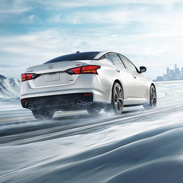 2026 Nissan Altima in white seen from behind driving in snowy landscape illustrating all-wheel drive. 