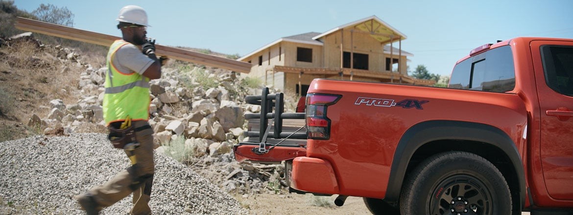 Worker loading wooden planks into the bed of a 2026 Nissan Frontier PRO-4X equipped with a bed extender