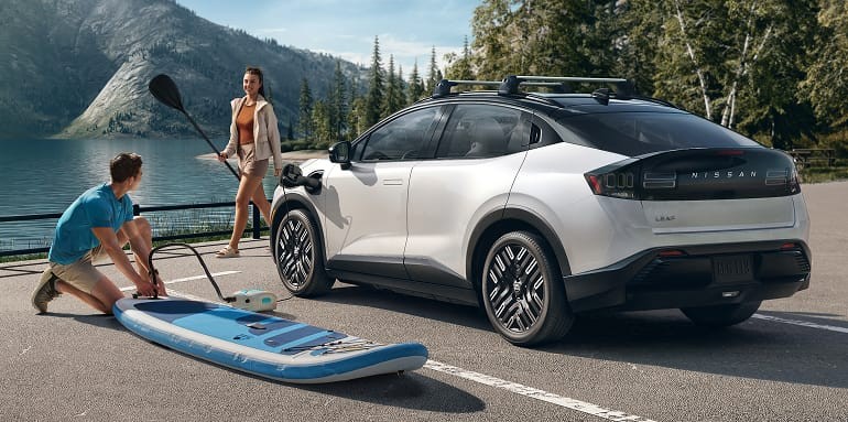 2026 Nissan LEAF 3/4 front view of a Leaf parked lakeside  showing using the vehicles 12-volt AC adapter to charge personal items and cargo