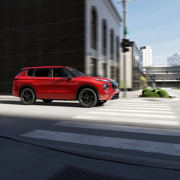 2026 Nissan Rogue Plug-in Hybrid side view driving on city street with buildings in the background.