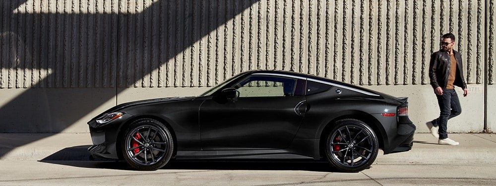 2026 Nissan Z in black, side view, parked in front of a concrete building with a pedestrian doing a double-take