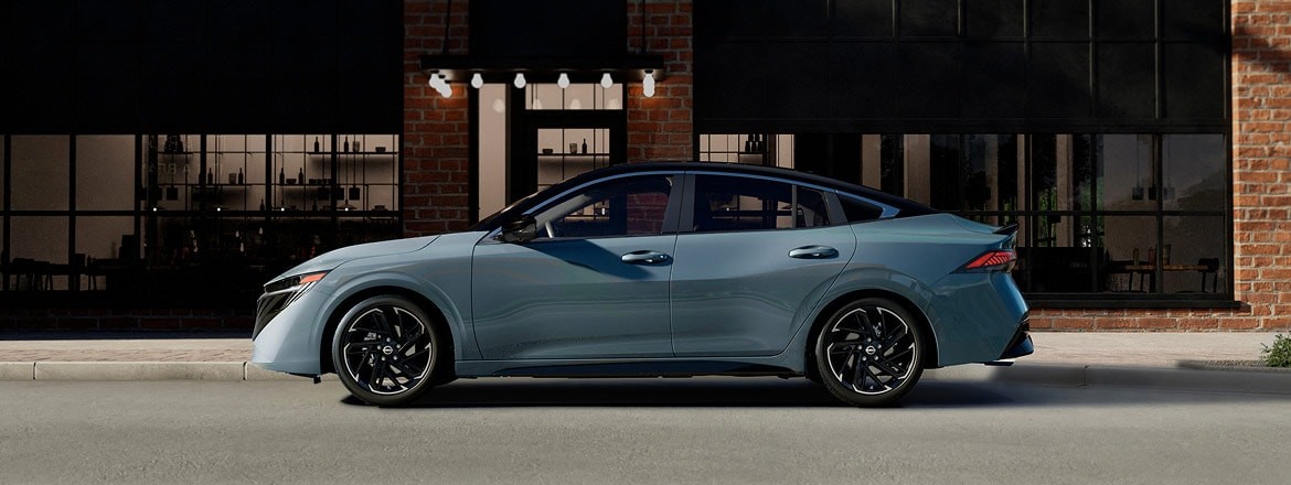 2027 Nissan Sentra side view parked in front of building with windows and subtle lighting at dusk.