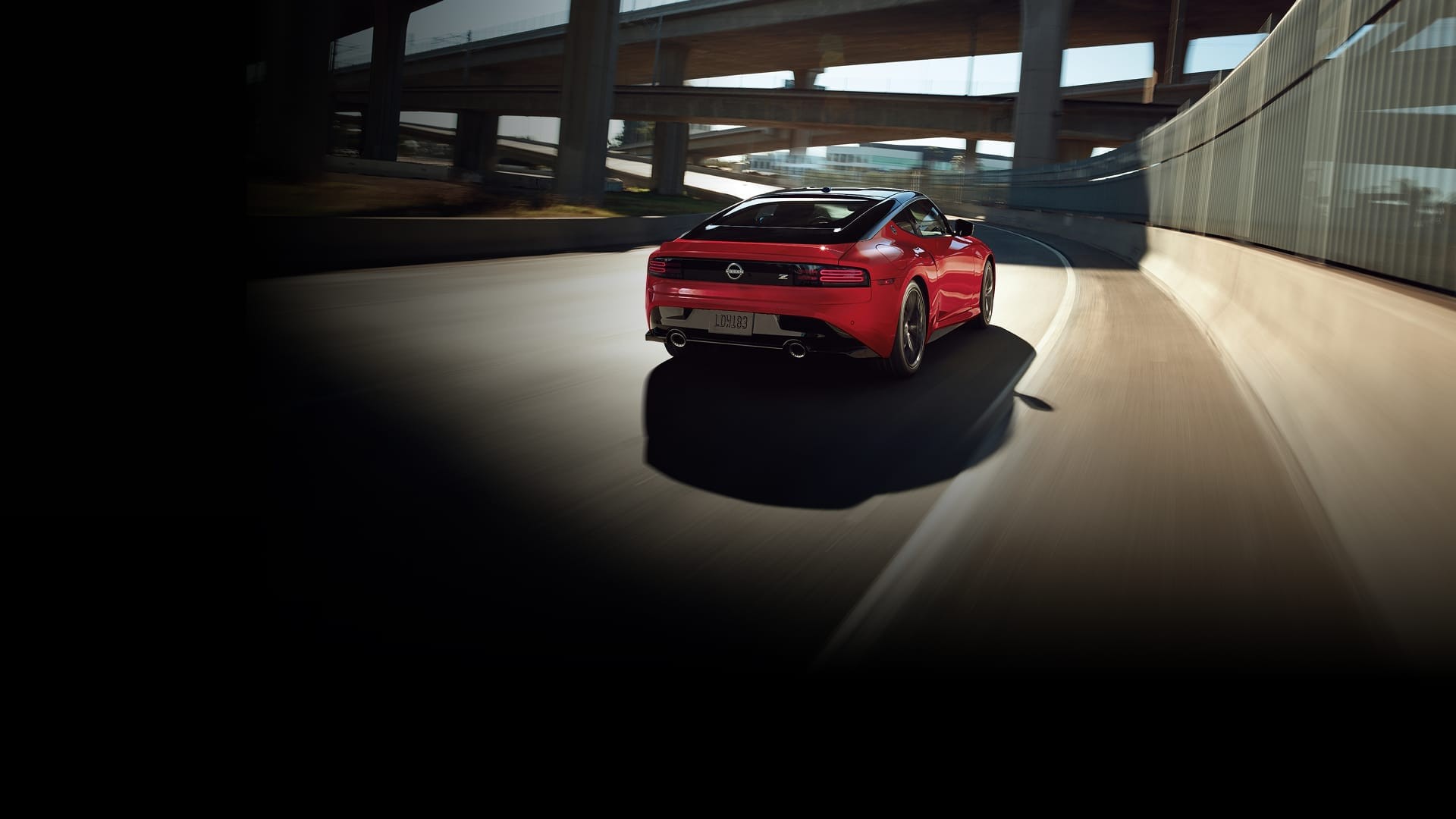 2027 Nissan Z in red, rear 3/4 view driving on city street.